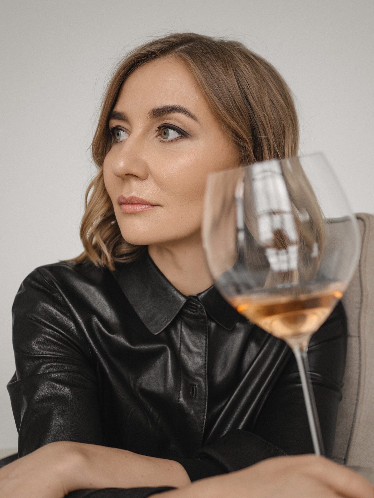 Liubov Leonova in a black leather shirt, a glass of rosé held in the foreground