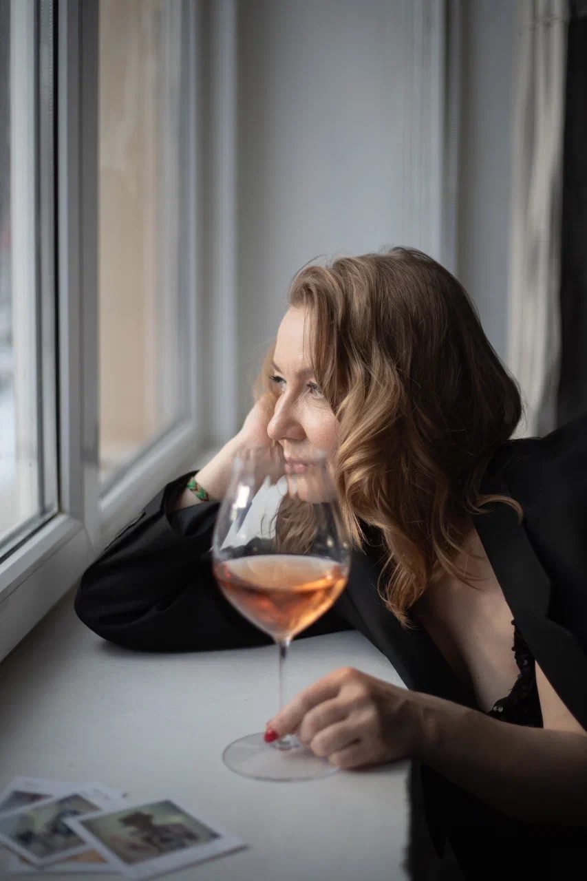 Liubov Leonova resting at a windowsill beside a glass of rosé and a scatter of photographs